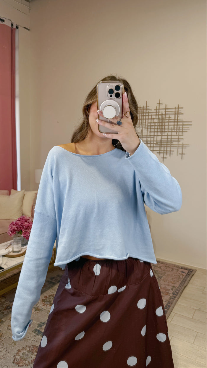 A woman takes a mirror selfie wearing a light blue long-sleeve knit top and a brown skirt with white polka dots in a cozy indoor room.