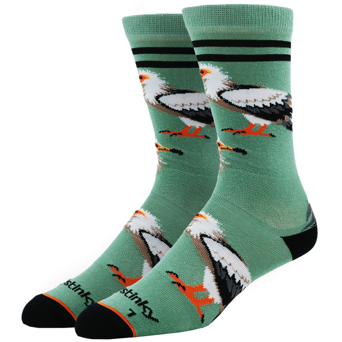 A pair of Stinks brand crew socks in sage green, featuring a graphic print of bald eagles and coqui frogs, with black stripes near the top and black heels and toes.