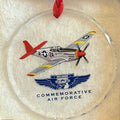 A round clear glass commemorative ornament hanging from a red ribbon, featuring a redtail P-51 Mustang and the Commemorative Air Force logo.