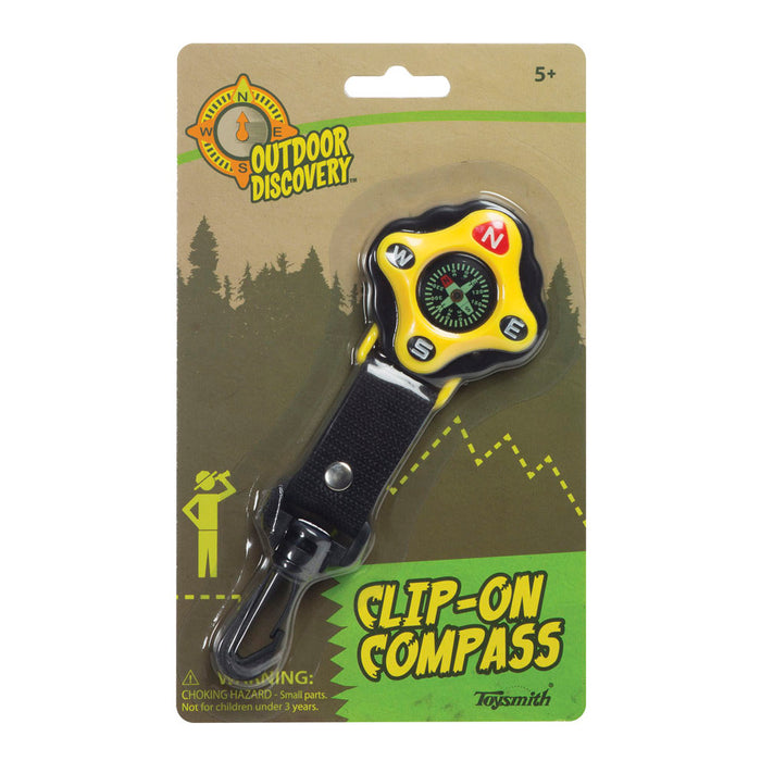 A Clip-On Compass with a bright yellow compass body attached to a black clip lanyard, packaged on a green and beige card with outdoor scenery illustrations.