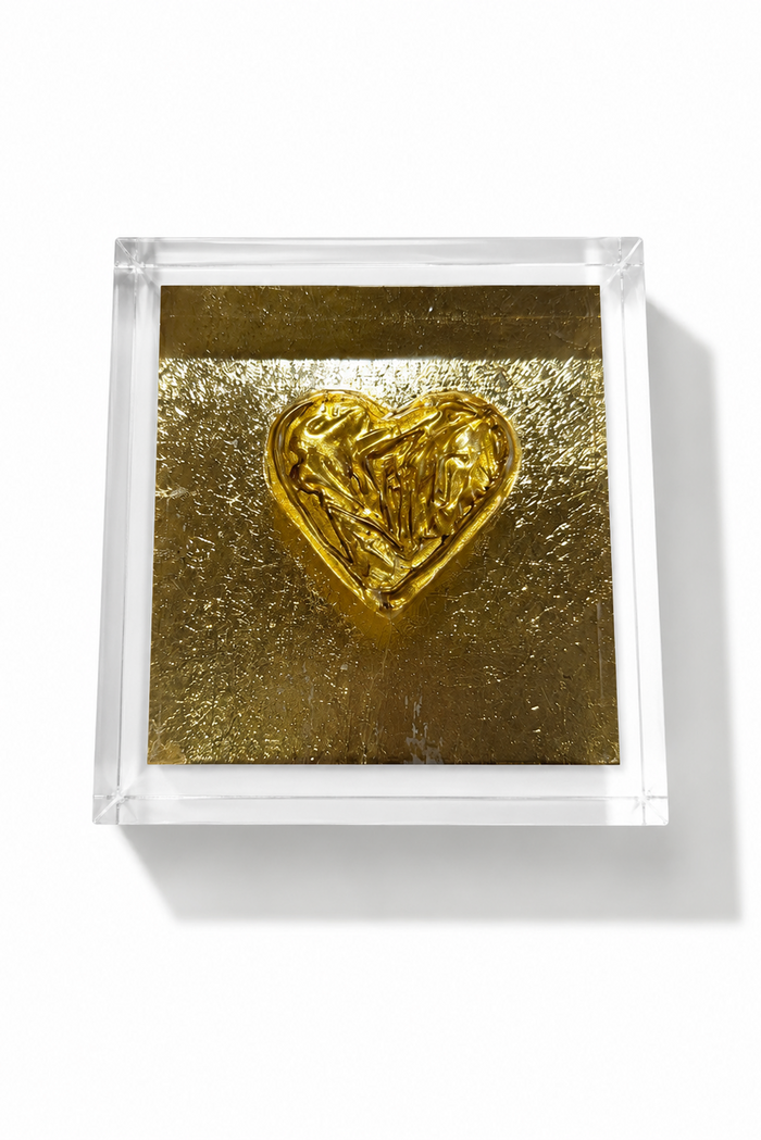 A square clear acrylic block containing a textured gold background and a raised metallic gold heart in the center, photographed on a clean white background.