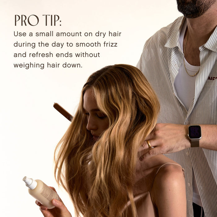 A woman with long, wavy blonde hair looks down while a man in a striped shirt styles her hair. In the lower left, she holds a bottle, and a text overlay reads: 'PRO TIP: Use a small amount on dry hair during the day to smooth frizz and refresh ends without weighing hair down.