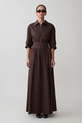Woman wearing a long brown dress with a belt on a white background