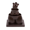 A sculpture reproduction of Rene Magritte's work featuring three hollow female forms stacked within each other on a square base, with a pair of robust thighs as a base. The sculpture is dark in color, with a matte finish.