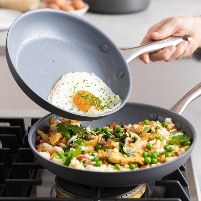 Fried egg being added to veggies and rice in a green ceramic nonstick skillet on a stove.