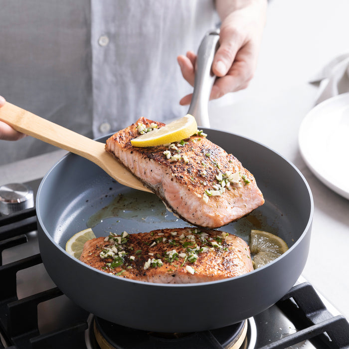 Salmon fillet with lemon being lifted from a gray ceramic nonstick pan using a spatula.