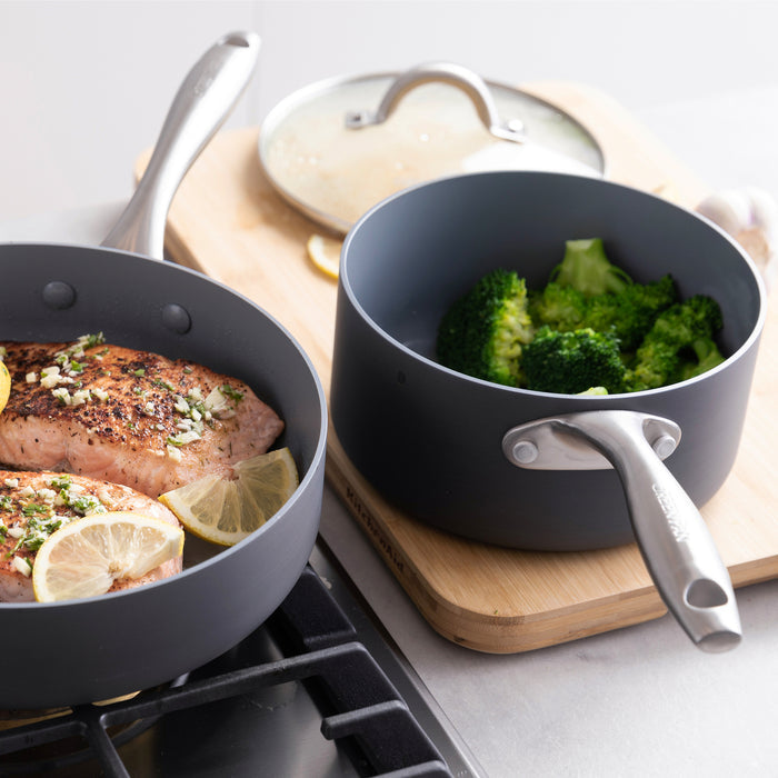 Two Lima ceramic nonstick pans, one with salmon and lemon, one with steamed broccoli, from a 12-piece cookware set.