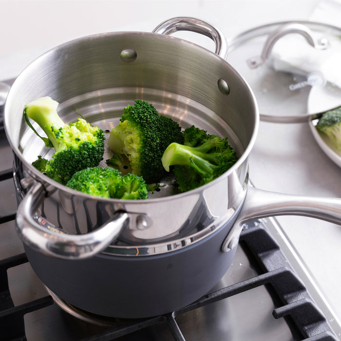 Green broccoli steaming in a ceramic nonstick pot on the stovetop, glass lid resting nearby.