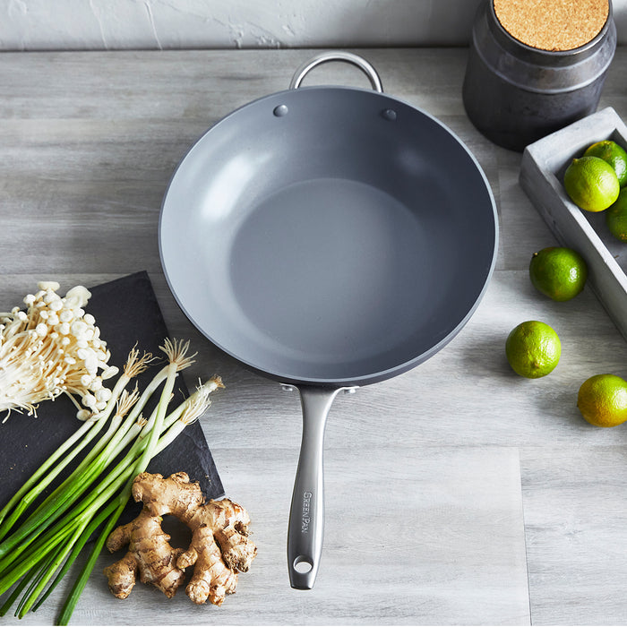 Gray ceramic nonstick wok, 12.5-inch size, on wood with ginger, green onions, mushrooms, and limes around it.