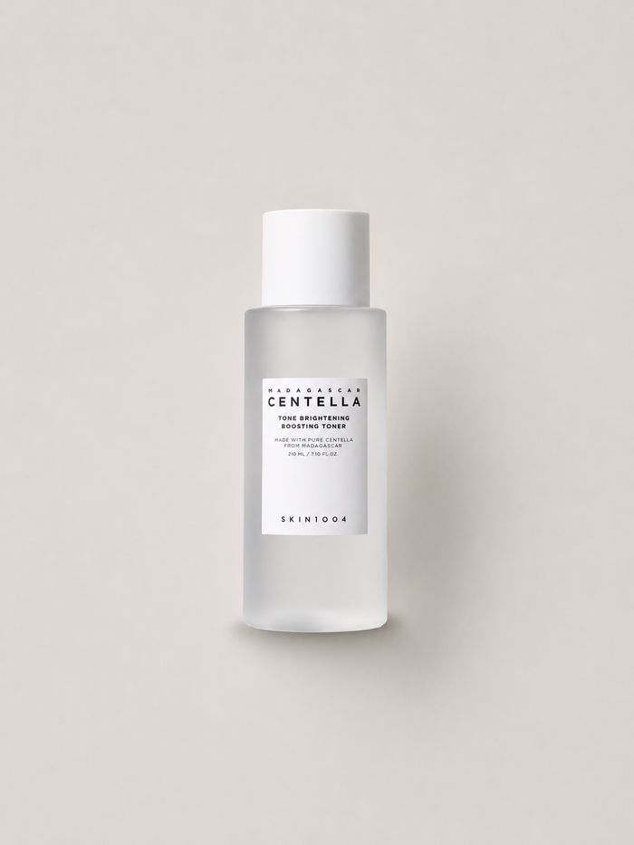 A bottle of Korean skincare toner -  SKIN1004 Madagascar Centella Tone brightening Boosting Toner, featuring a frosted glass bottle and a white cap, set against a solid light beige background. 210 ml.