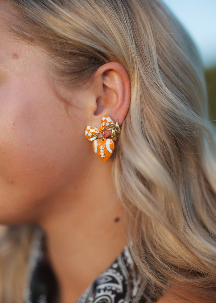 A close-up side profile of a woman with blonde hair wearing a small orange and white patterned hoop earring with gold-toned metal.