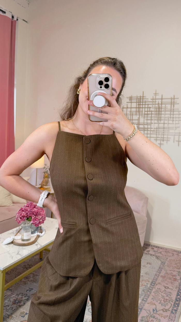 A woman takes a mirror selfie wearing a matching brown pinstripe vest and trousers set. The vest features a square neckline, three front buttons, and a structured silhouette, paired with matching wide-leg trousers.