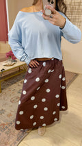 A person taking a mirror selfie in an indoor room, wearing a light blue off-the-shoulder long-sleeve top and a brown skirt with large light blue polka dots.