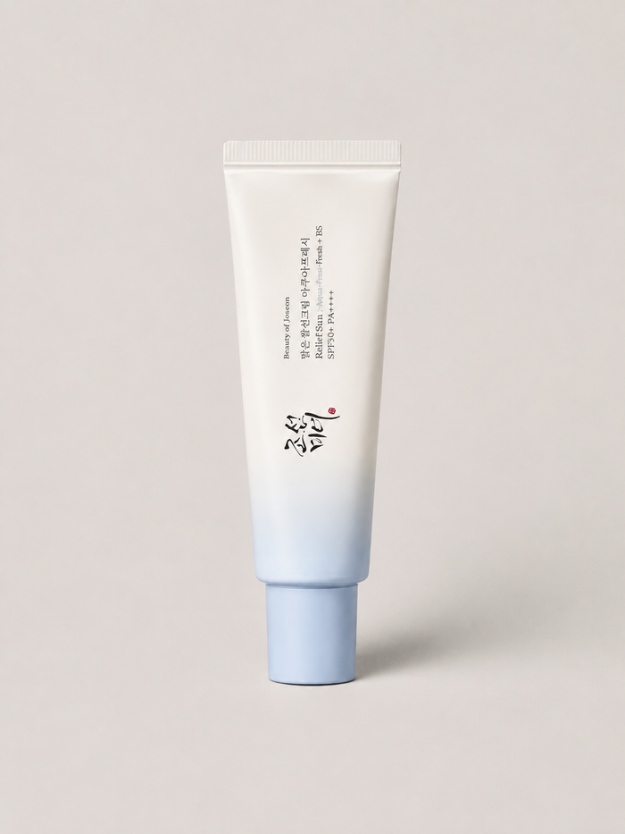 A korean skincare SPF cream tube with a white to light blue gradient design, standing upright against a neutral light gray background. The tube features Beauty of Joseon Relief Sun Aqua-Fresh: Rice + B5. SPF 50+, 50 ml.