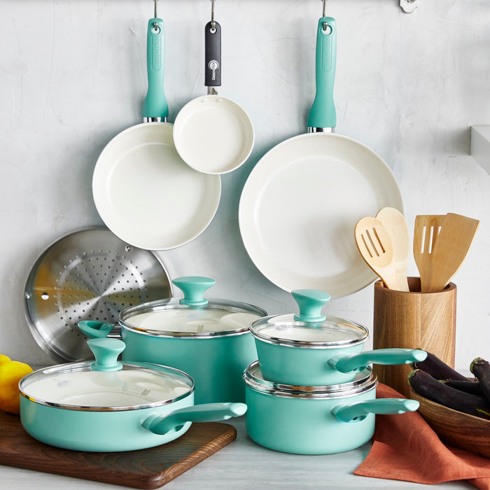 Turquoise ceramic 16-piece cookware set with glass lids and utensils displayed on a kitchen counter and wall.