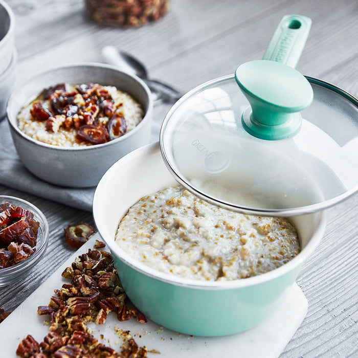Turquoise ceramic nonstick pot from 16-piece set next to a bowl of oatmeal topped with dates and pecans.