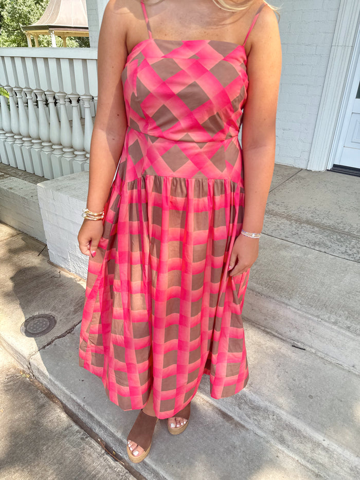 A woman wearing a sleeveless midi dress with a pink and brown geometric lattice pattern, standing on concrete steps outdoors.
