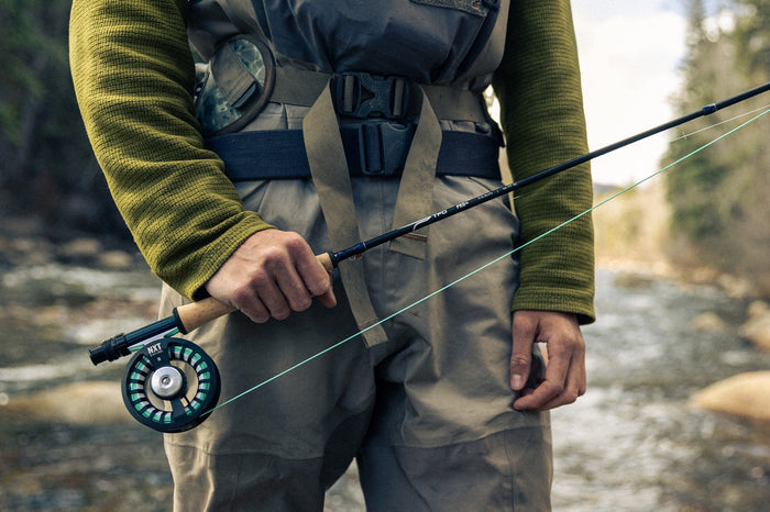 Person holding a fishing rod by a stream