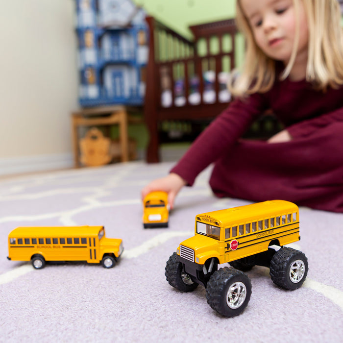 A young child in a maroon dress sits on a carpeted floor, playing with three Toysmith Monster School Bus toys by Toysmith; a crib and bookshelf are in the softly lit background.