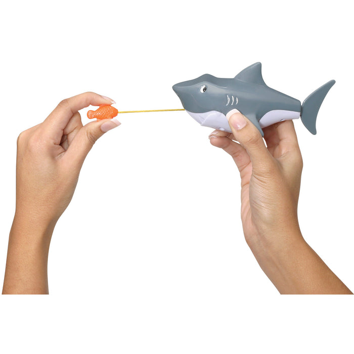 A person holds the Tub Time Pull-String Shark bath toy by Tub Time, with a string attached to an orange fish, as if the shark is catching it. The background is plain white.