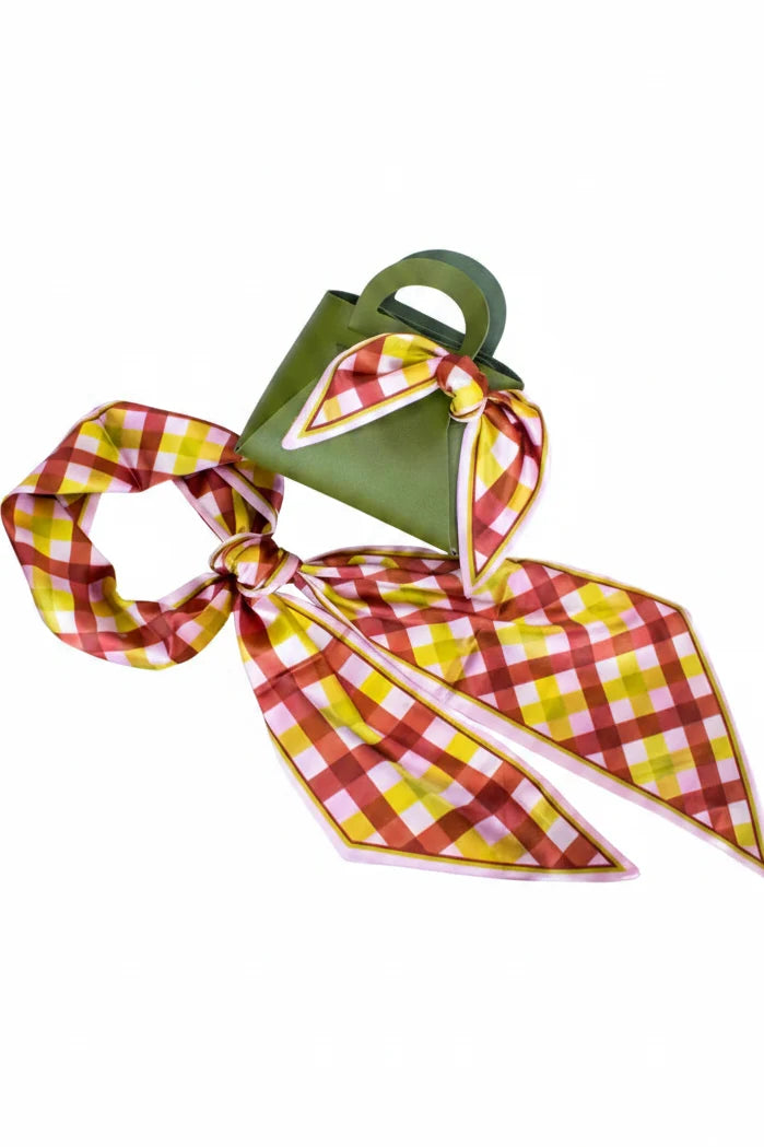 A green handbag with a matching plaid scarf tied around it, photographed on a plain white background. The scarf has a red, yellow, and white check pattern with a thin gold border, and the bag has gold lettering that reads 'LOVING VALTS'.