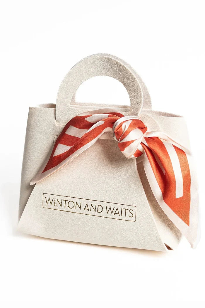 A small structured cream-colored handbag with a top handle, featuring a red and white striped silk scarf tied in a bow around the neck. The brand name 'WINTON AND WAITS' is printed on the front.