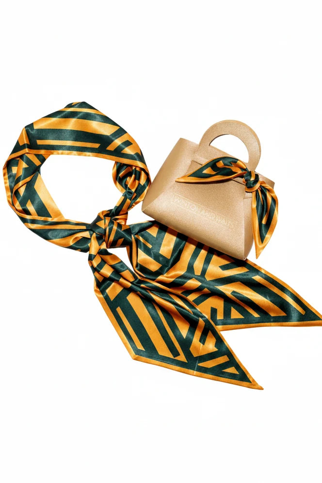 Beige handbag with a green and orange patterned scarf draped over it on a white background