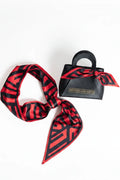 Red and black patterned scarf with a black handbag on a white background